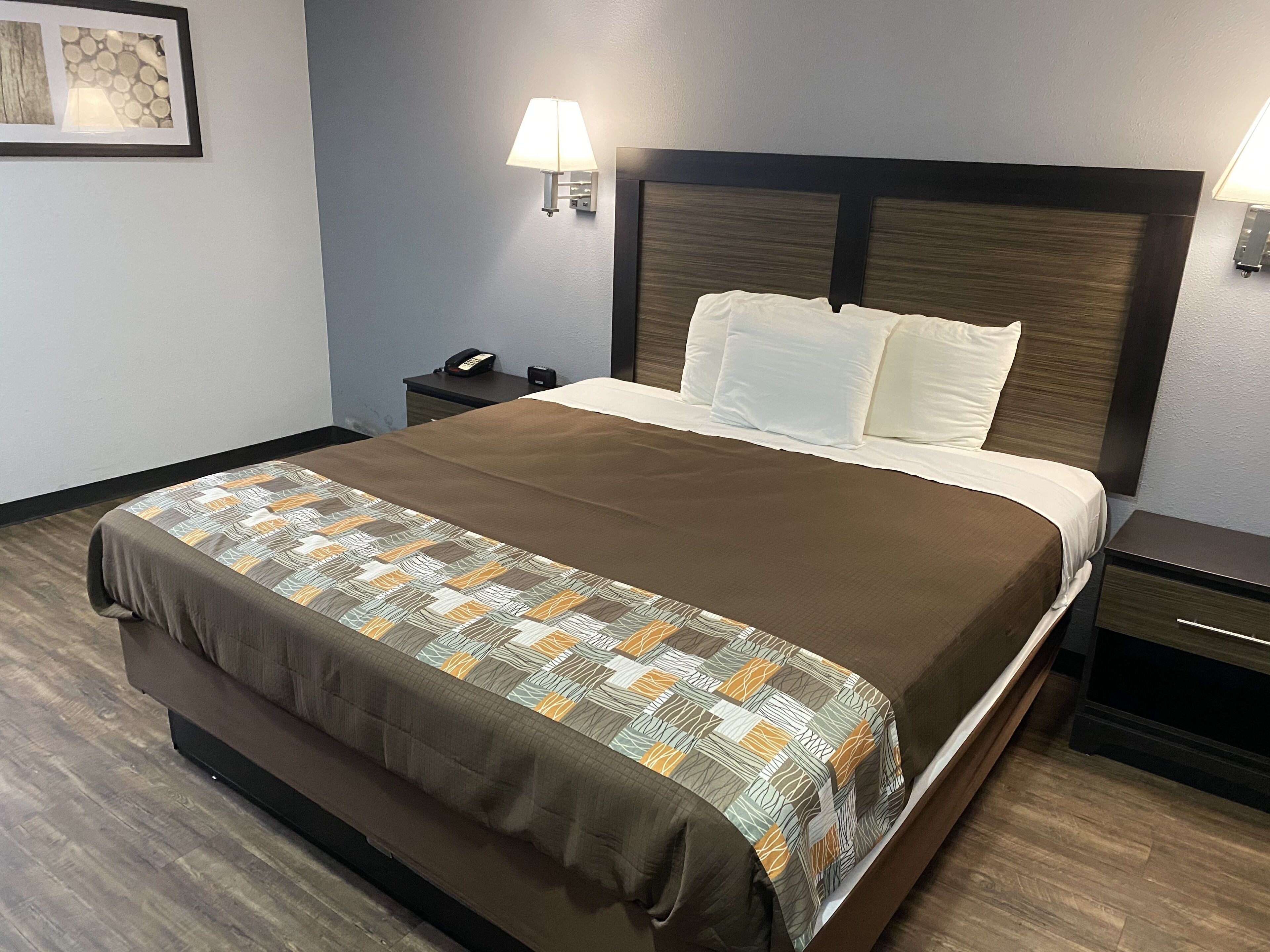 Una camera d'albergo con un letto grande, un comodino con telefono, una lampada e un quadro appeso al muro.