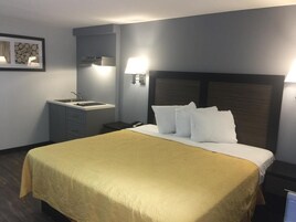 Habitación de hotel con una cama grande, una mesita de noche, una lámpara, un espejo y un pequeño escritorio con una silla.
