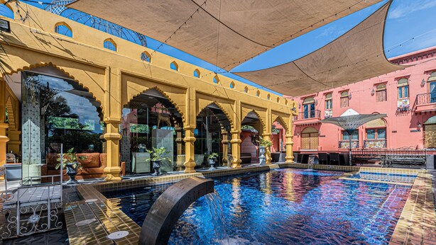 Uma área de piscina com piso cerâmico, um elemento aquático e uma galeria coberta com arcos.