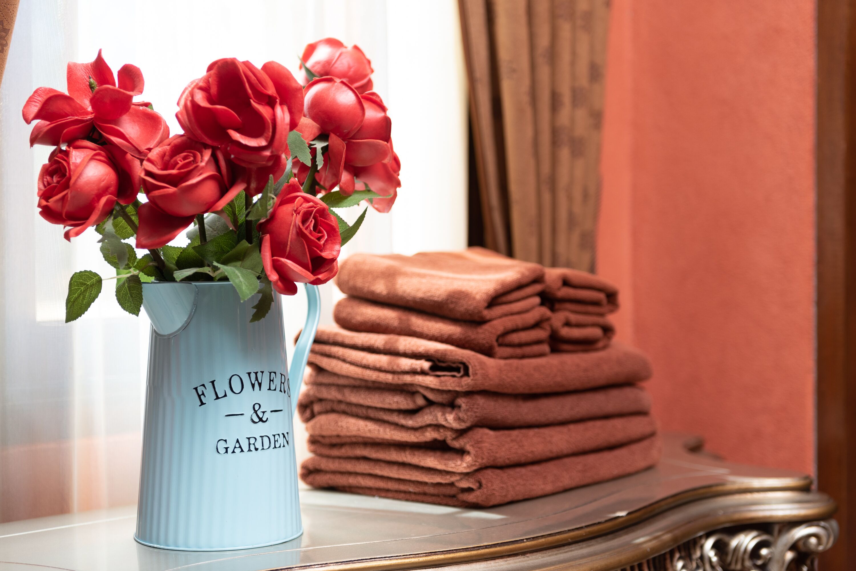 Un vaso blu con rose rosse e una pila di asciugamani piegati su un tavolo.