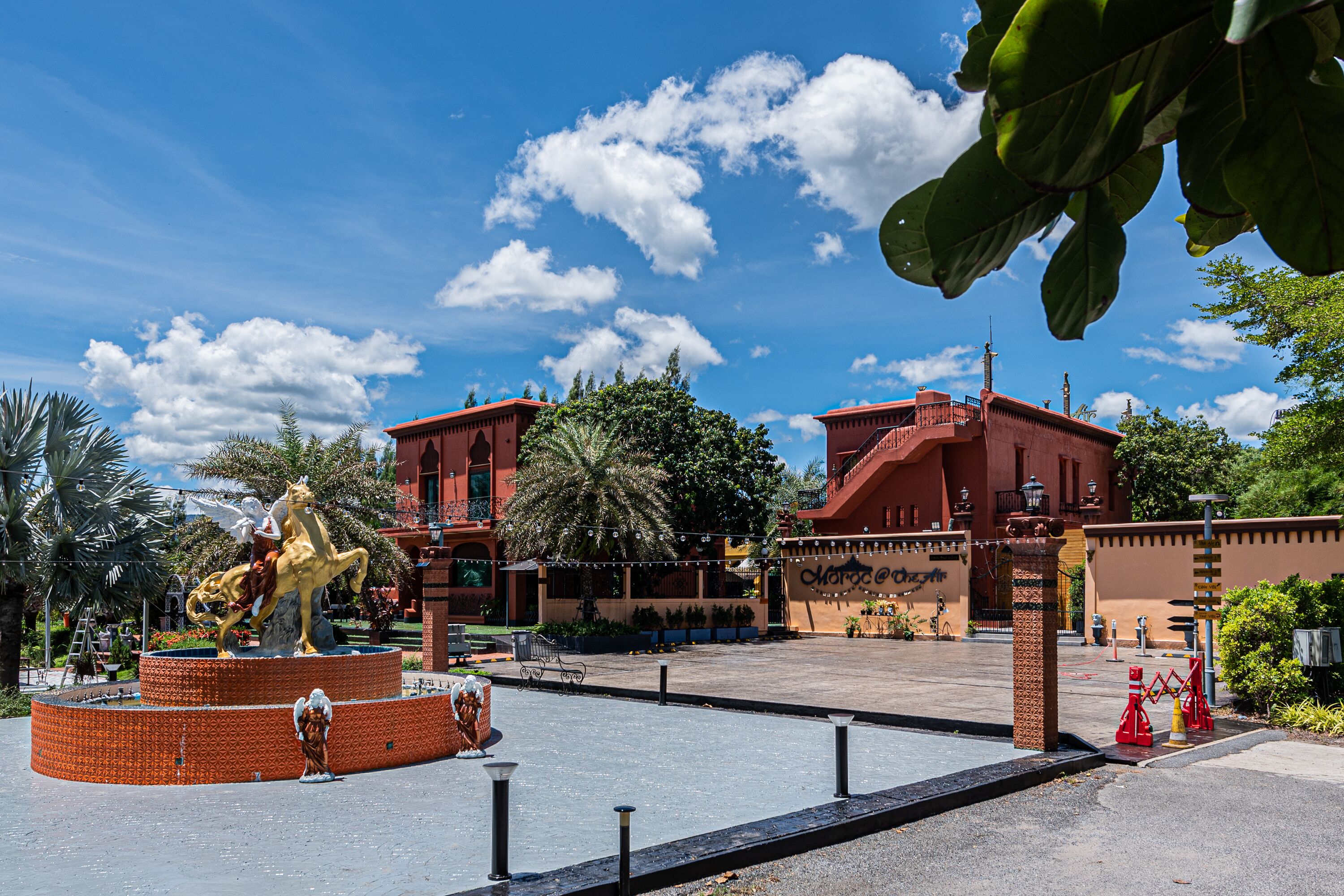 A courtyard with a fountain, palm trees, and a building with a red facade.