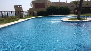 A swimming pool with clear blue water, surrounded by a low fence, and adjacent to a building with a flat roof and beige walls. - Penthouse with sunny roof terrace, seaview, close to bars/restaurants, air con (Mijas)