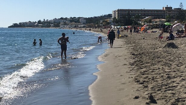 A beach with people walking and swimming, buildings in the background, and a clear sky. - Penthouse with sunny roof terrace, seaview, close to bars/restaurants, air con (Mijas)