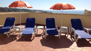 A terrace with four blue lounge chairs and two red umbrellas, overlooking a coastal view. - Penthouse with sunny roof terrace, seaview, close to bars/restaurants, air con (Mijas)