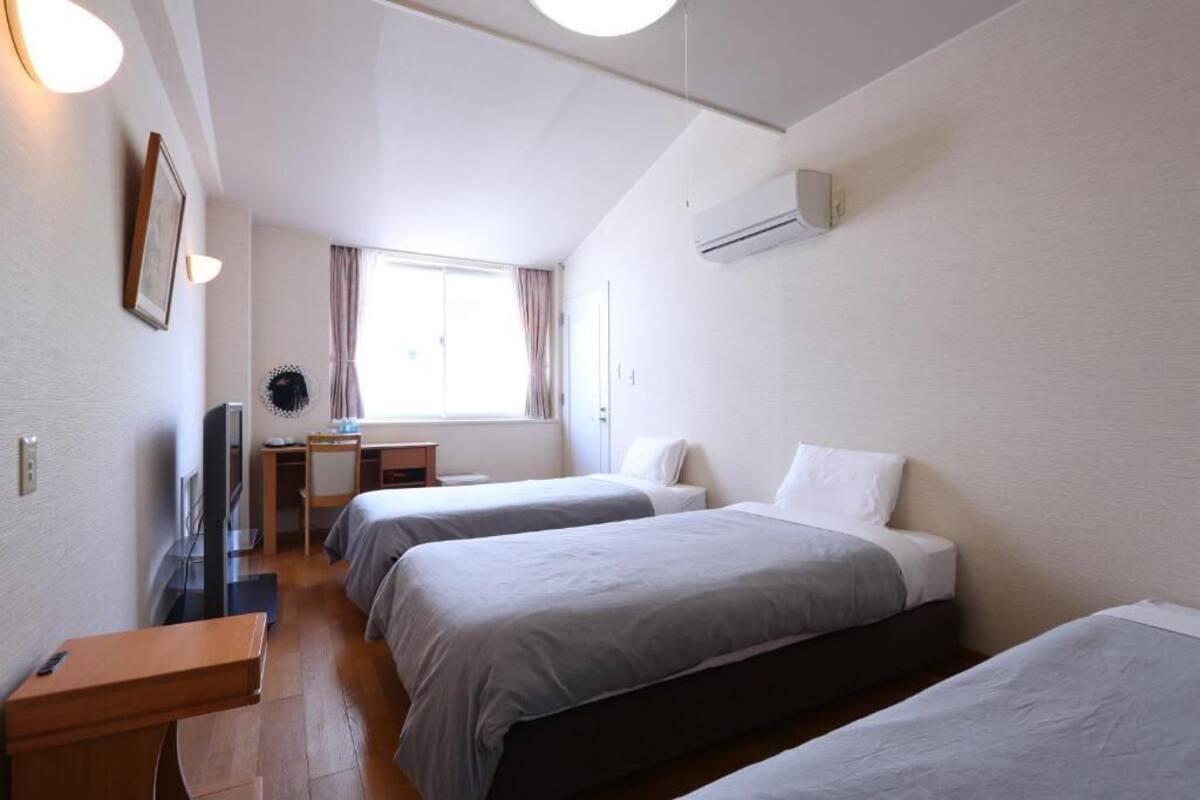 A hotel room with two single beds, a desk with a chair, a TV, and a window with curtains.
