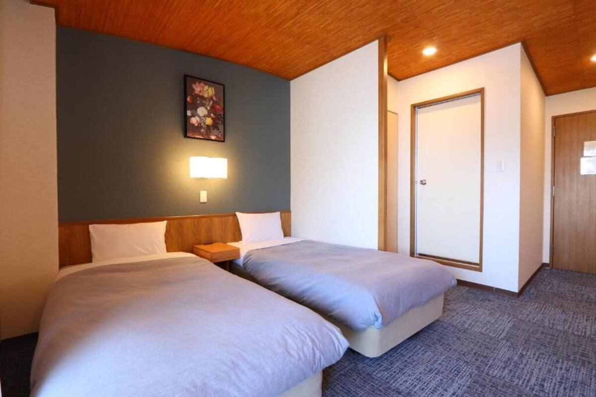 A hotel room with two beds, a wooden ceiling, a framed picture on the wall, and a door.