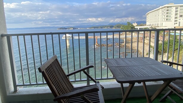 Uma varanda com vista para o mar, uma cadeira e uma mesa.