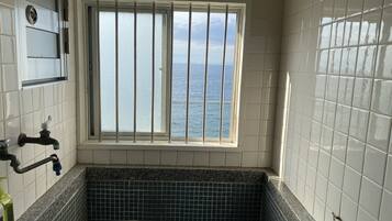 Une salle de bain donnant sur la mer grâce à une fenêtre à barreaux, un lavabo avec un robinet et un mur recouvert de carreaux.