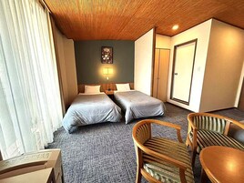 Una habitación de hotel con dos camas, techo de madera, una pequeña mesa y una silla.