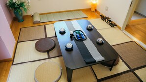Um espaço com esteiras de tatame, uma mesa baixa, almofadas, uma pequena mesa redonda e um objeto decorativo.