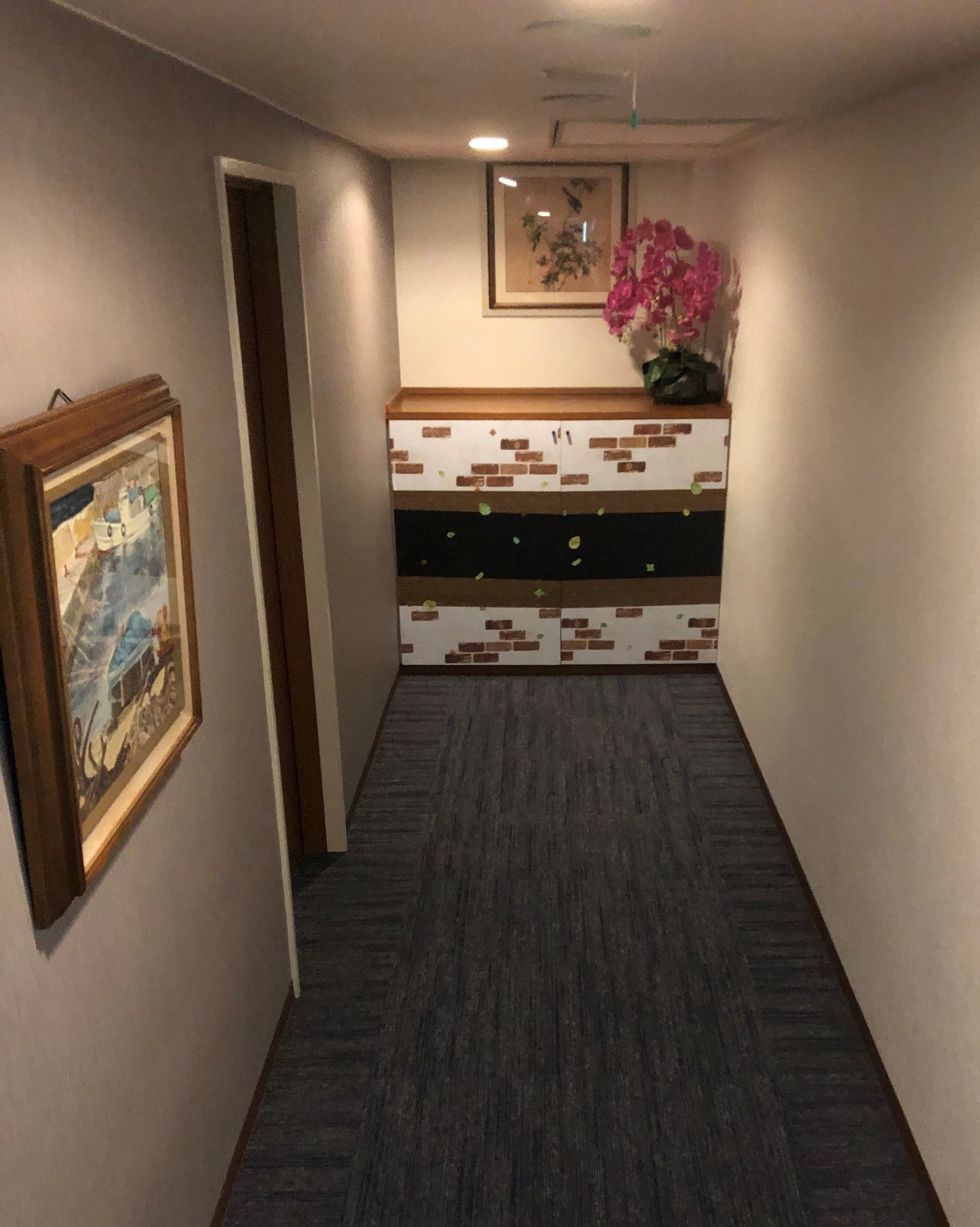 Un couloir avec un meuble mural décoré, un tableau encadré et une plante en pot.