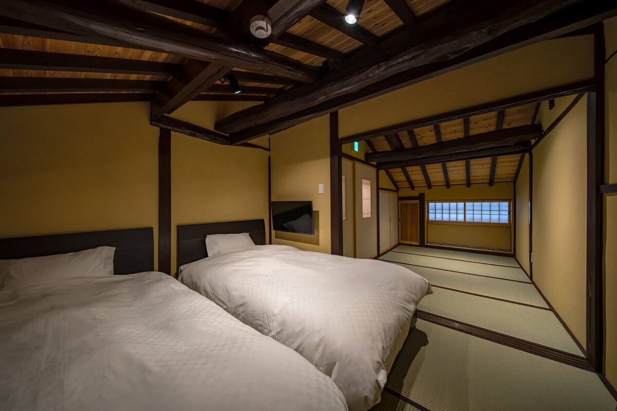 Una habitación tradicional japonesa con suelo de tatami, dos camas y un puertas correderas que dan a un balcón.