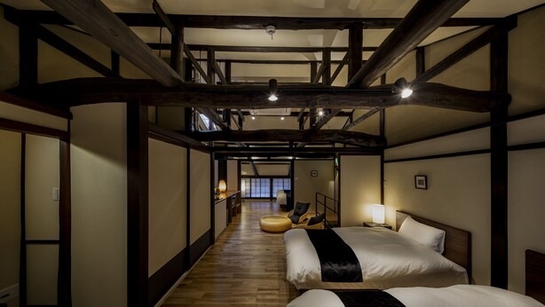 Une chambre d’hôtel avec un plancher en bois, deux lits, un canapé et une vue sur un intérieur japonais traditionnel.