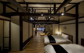 A hotel room with a wooden floor, two beds, a sofa, and a view of a traditional Japanese interior. - Obama Machiya Stay (Obama)