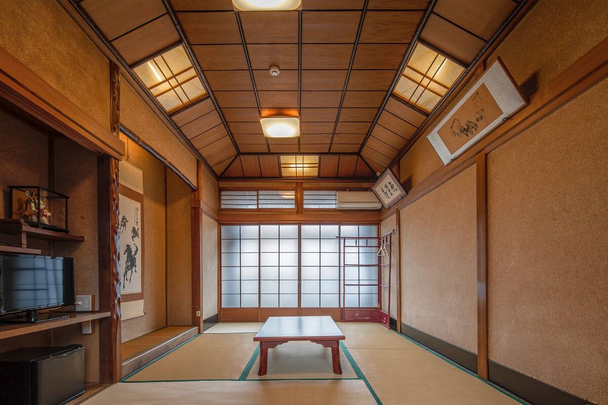Una habitación japonesa tradicional con suelo de tatami, una mesa de madera baja, puertas correderas y un televisor.