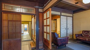 Un intérieur japonais traditionnel avec un sol recouvert de tatamis, une porte coulissante et un coin salon comprenant un canapé et des fauteuils.