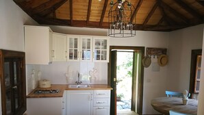 Une cuisine chaleureuse avec des meubles blancs, un évier et une cuisinière. On y trouve également un coin repas avec une table ronde et des chaises bleues.