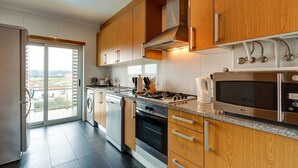 Een moderne keuken met houten kastjes, roestvrijstalen apparatuur en een groot raam met uitzicht op de omgeving.