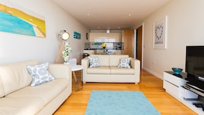 Una sala de estar moderna con un sofá beige, un tapete azul y un mueble para televisor.