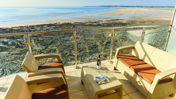 Un balcón con mobiliario de mimbre y vista a una playa y la costa.