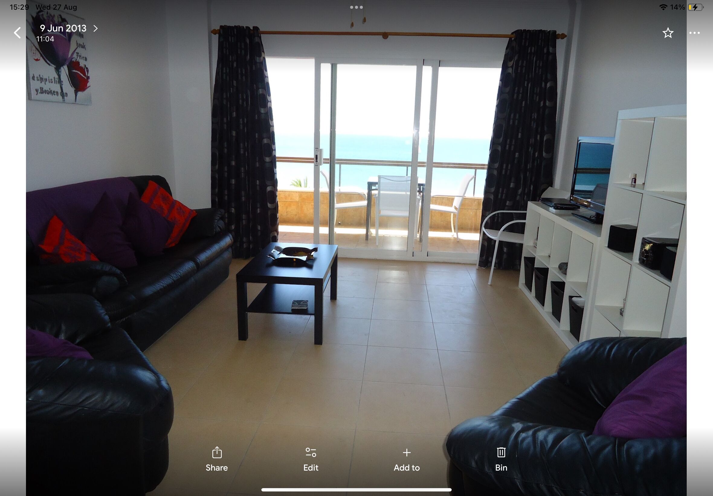 Una sala de estar con un sofá, una mesa de centro, un escritorio con una computadora y vista al mar a través de una puerta corrediza.