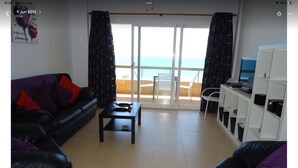 A living room with a sofa, a coffee table, a desk with a computer, and a view of the sea through a sliding door. - Apartment With Stunning Sea Views And Vision Of The Rock Of 🇬🇮Gibraltar (Estepona)