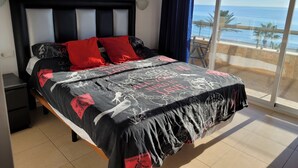 A bedroom with a bed, a nightstand, a large window with a view of the sea, and a balcony with a table and chairs. - Apartment With Stunning Sea Views And Vision Of The Rock Of 🇬🇮Gibraltar (Estepona)
