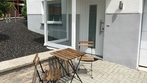 Un patio exterior con una mesa y sillas de madera, una puerta de vidrio y una pared blanca.