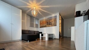 Una sala moderna con suelo de madera, un sofá negro, una mesa de centro blanca y un cuadro abstracto grande en la pared.