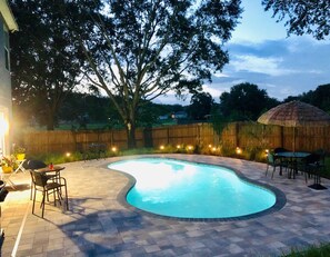 Un jardin avec une piscine, des meubles de patio et un parasol en chaume.