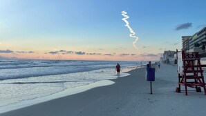 A beach with a lifeguard tower, a clear sky, and a person walking. - Walk to Beach! Family Beach House, Game room!  Sunset View! (Daytona Beach)