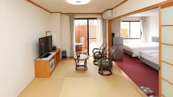 A hotel room with a TV, a small table with chairs, a bed, and a sliding door to a balcony.