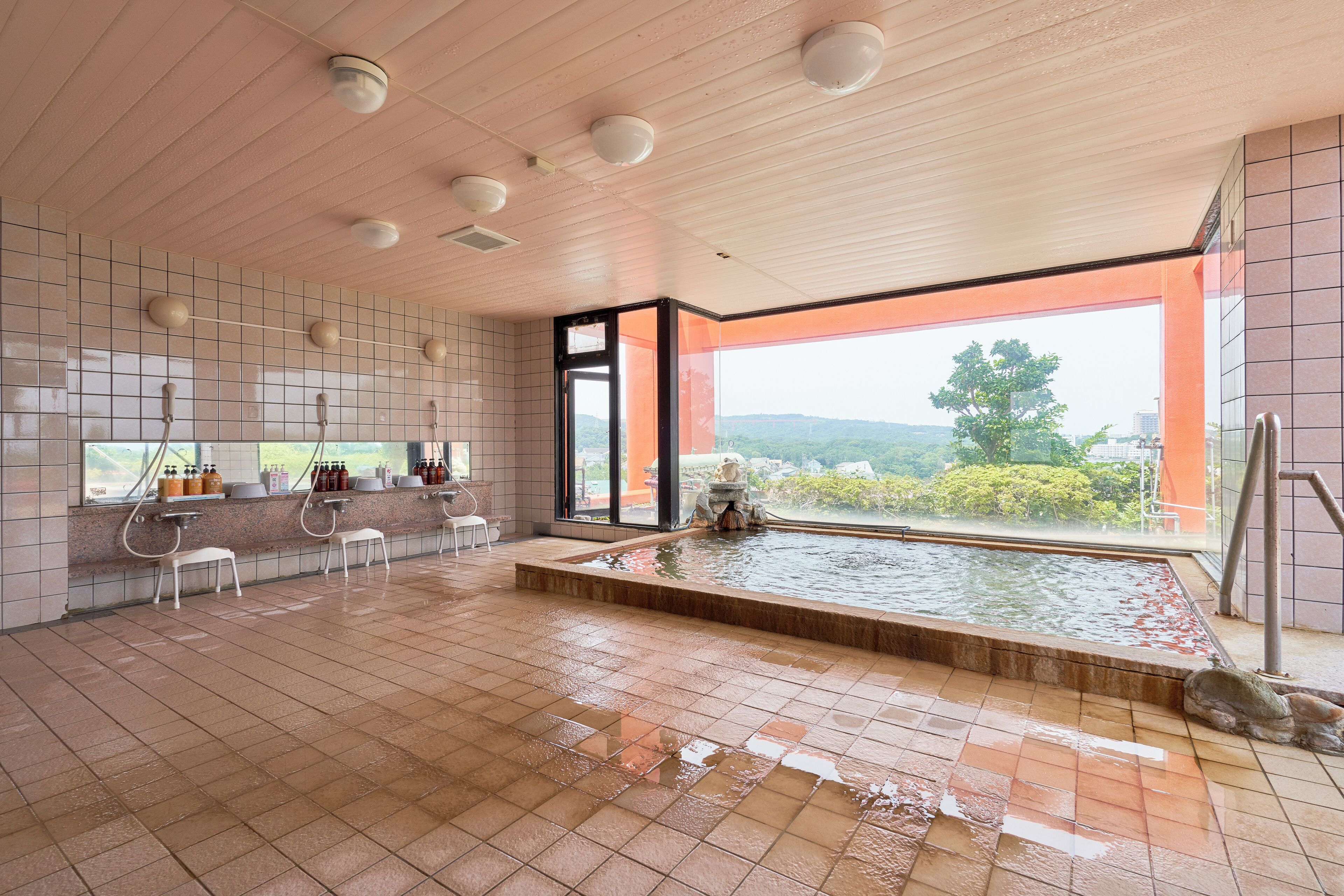 A spacious indoor pool area with a view of the outdoors, tiled walls, and a seating area with chairs.