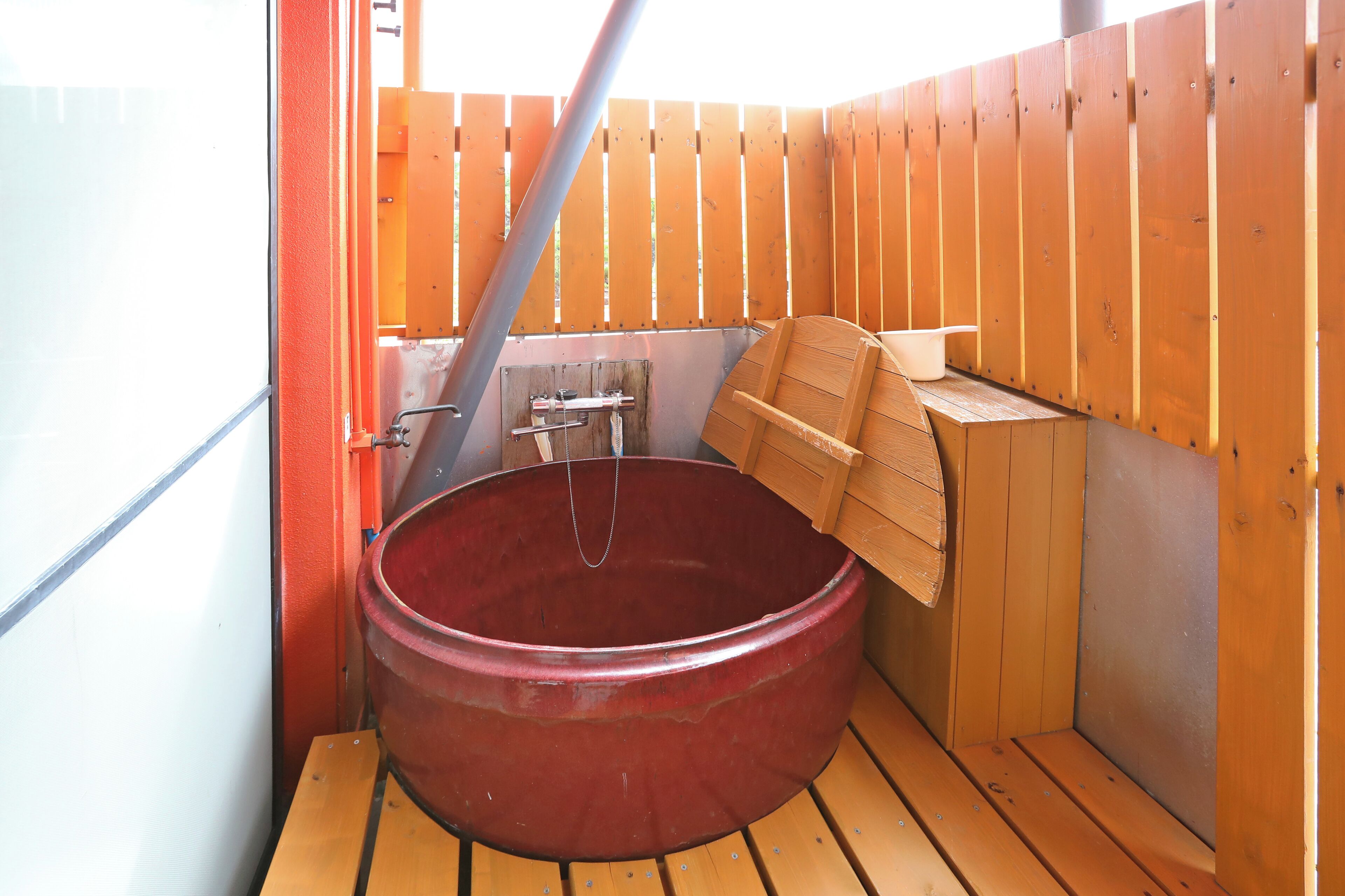 A wooden sauna with a large red tub, a bench, and a wooden bench on the floor.