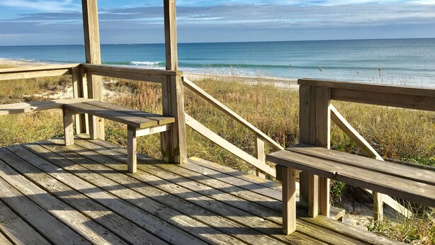 Eine Holzterrasse mit Bänken mit Blick auf einen Strand.