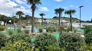 Ein Golfplatz mit Palmen, einer Grünfläche und einem Sandstrand im Hintergrund.