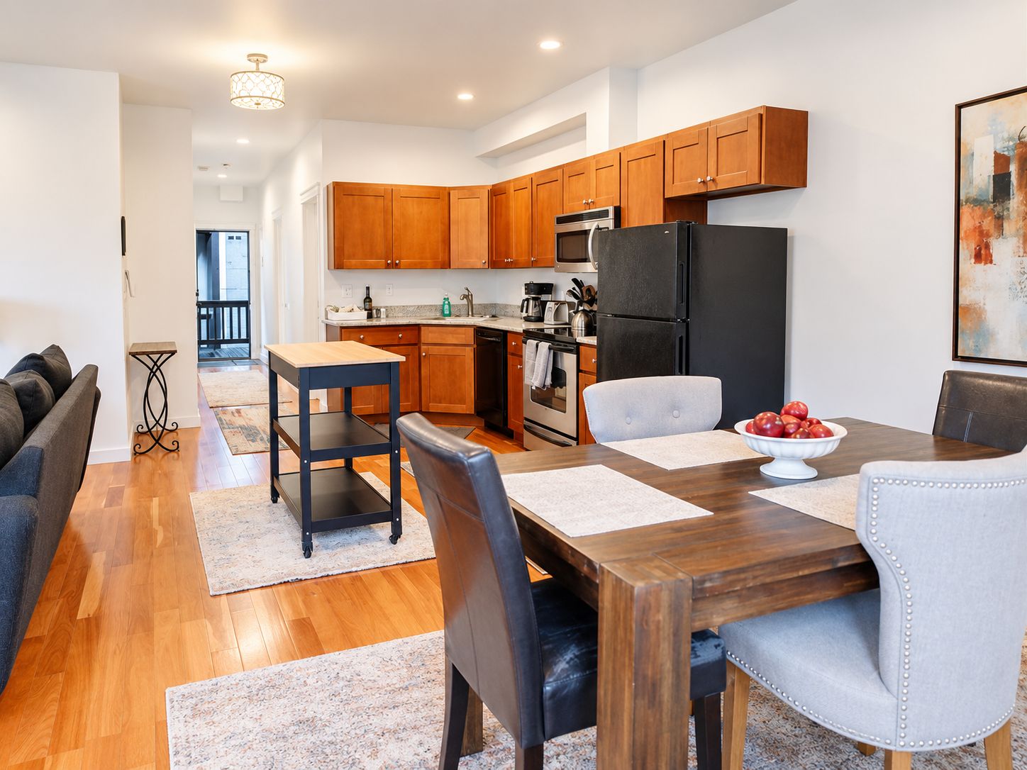 A modern kitchen with wooden cabinets, a black refrigerator, and a dining area with a wooden table and chairs.