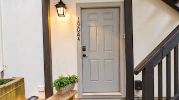 A front door with a number plaque, a wall-mounted light fixture, a potted plant, and a bench.