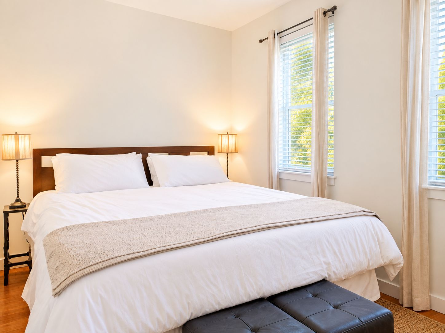 A neatly made bed with white linens and a beige throw blanket, flanked by two bedside lamps.