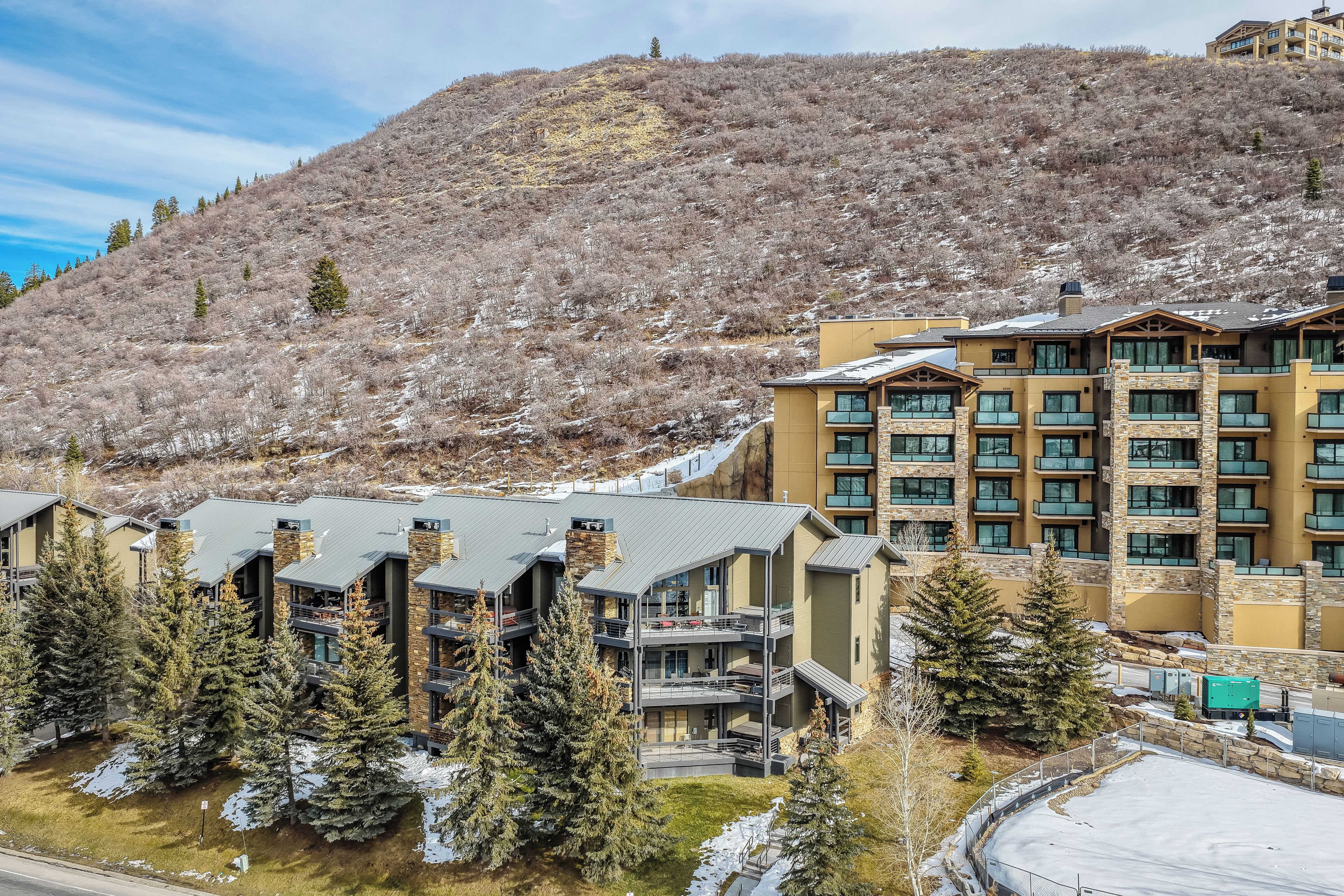 A multi-story hotel with a mountain backdrop, featuring balconies and a ski slope view.