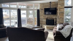 A modern living room with a stone fireplace, large windows, and comfortable seating. - Powder Run Premier Unit - All NEW Corner unit with views, Private Hot Tub !! (Park City)