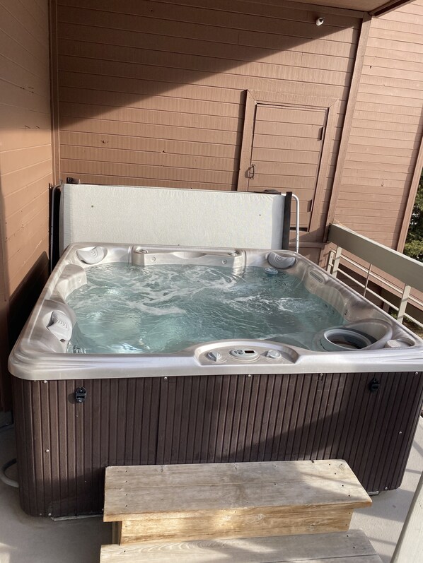 A hot tub with a wooden exterior and a metal frame, positioned outdoors against a brick wall.