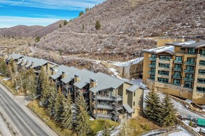 A modern hotel with multiple balconies, a ski slope in the background, and a clear sky. - Powder Run BEST Unit - NEW Corner unit with views up slopes and PRIVATE HOT TUB! (Park City)