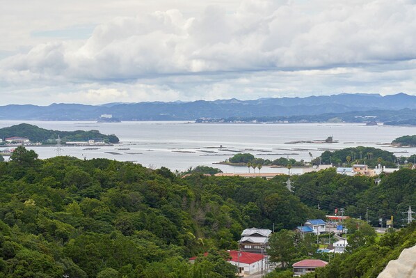 A coastal town with dense greenery, a body of water, and distant mountains. - Shiki no Sato Yuraku (Shirahama)