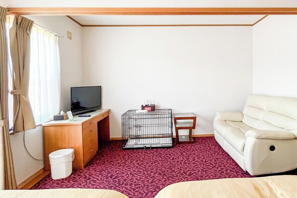 A compact room with a bed, a desk with a television, a small table, a white sofa, and a pet cage. - Shiki no Sato Yuraku (Shirahama)