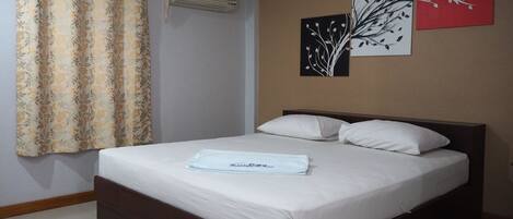 Una cama bien hecha con un edredón blanco y almohadas, una cortina con estampado floral y dos cuadros con ramas.