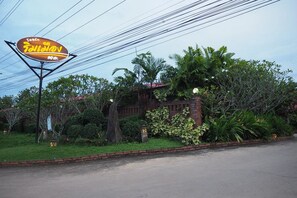A restaurant sign with a logo and name, surrounded by lush greenery and a brick building.