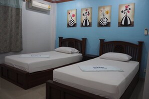 A hotel room with two single beds, a wall-mounted air conditioner, and three floral paintings on the wall.