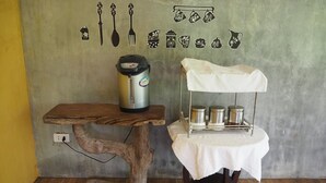 A rustic kitchen with a wooden table, a coffee maker, and a shelf with metal containers. - Rimmueng Resort (Phanom Sarakham)