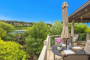 Un área de estar al aire libre techada con una mesa para dos, rodeada de exuberante vegetación y una vista panorámica de un lago y colinas.